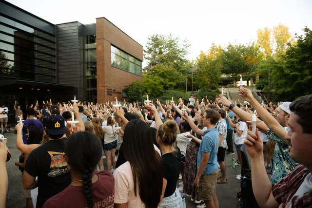 Students worshipping outdoors with raised hands outside an academic building