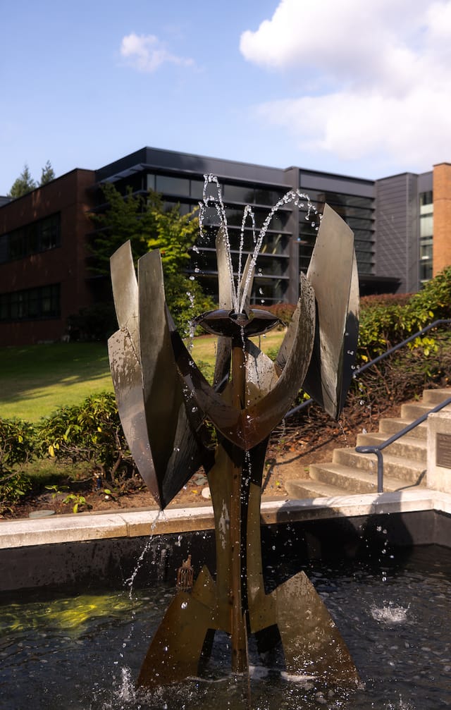 A sculptural fountain on the campus hillside below a modern academic building