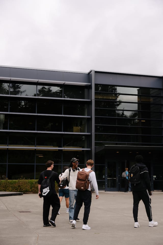 Students walking past a glass-fronted academic building on a sunny day