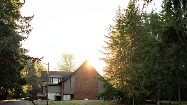 Sunrise behind a brick A-frame building framed by tall evergreens