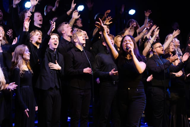 A choir dressed in black sings with raised hands as a soloist leads at the microphone