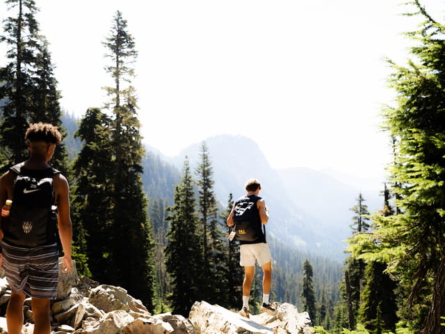 Two students hiking near Snow Lake, looking out over a misty mountain valley lined with evergreens